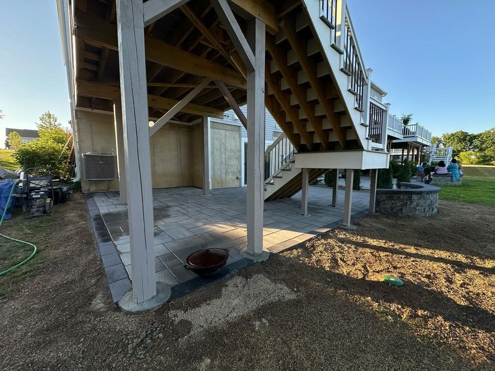 Under-deck patio with paver flooring, stairs, and landscaped yard. Ideal outdoor living space.