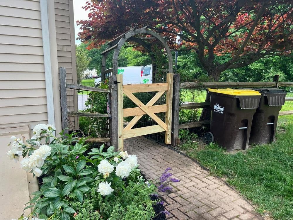 Wooden garden gate with flowers and trash bins in a landscaped yard.